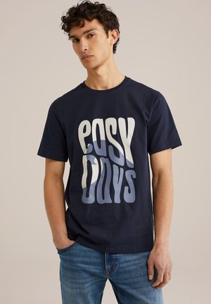 Marineblå bomulds T-shirt med et bølget hvidt grafisk design, der står "EASY DAYS". Rund halsudskæring, korte ærmer, glat tekstur.