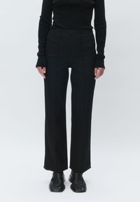 Black high-waisted trousers with a straight-leg design, featuring sleek lines and a smooth, textured fabric. Paired with black shoes.
