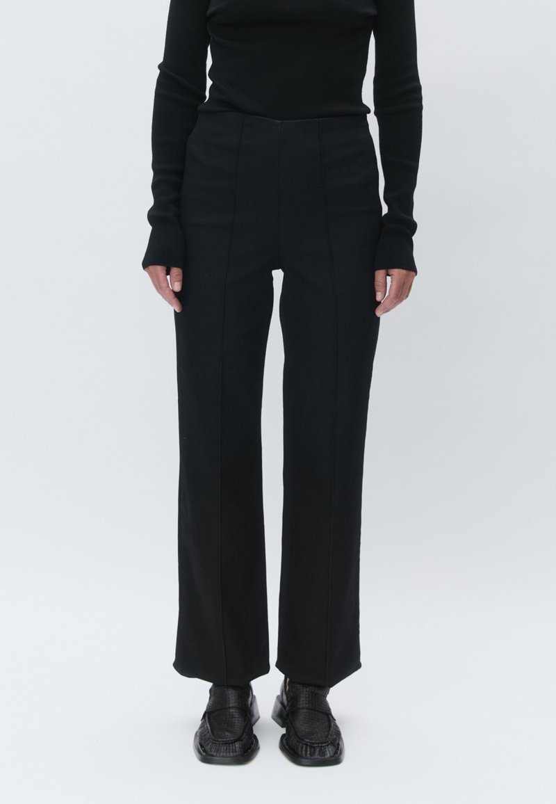 Black high-waisted trousers with a straight-leg design, featuring sleek lines and a smooth, textured fabric. Paired with black shoes.