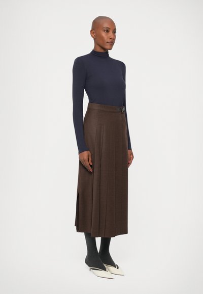 Marineblå turtleneck-top parret med en brun plisseret midi-nederdel med sideslids, grå strømpebukser og spidse hvide hæle.