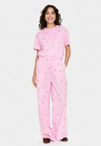 Roze tweedelige pyjama set bestaande uit een t-shirt en brede broek, beide met een rood hartpatroon, gemaakt van zachte, lichte materialen.