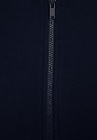 Gros plan d'une fermeture éclair noire fermée sur un tissu foncé, centrée verticalement.
