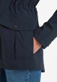 Navy blue waterproof jacket featuring a cinched waist, large front pocket with flap, and a button closure. Smooth fabric, casual design.