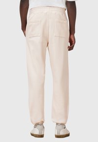 Lichtroze sweatpants met een elastische tailleband, twee achterzakken en elastische boorden bij de enkels, gecombineerd met witte sneakers.