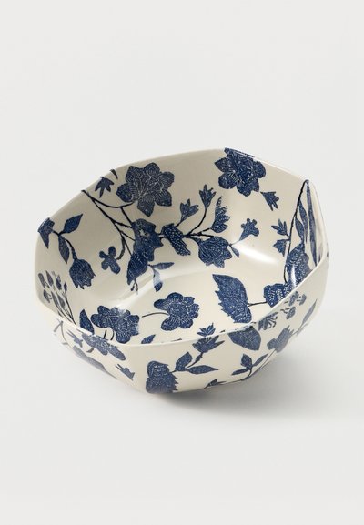 Λευκό κεραμικό μπολ με μπλε λουλουδένια σχέδια και πολυεδρικό, γωνιώδες σχήμα σε απλό φόντο.