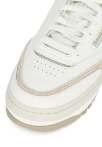 Fehér bőr sneaker texturált bézs részletekkel, kerek orr, perforált díszítéssel az orrdozon, és lapos fehér fűzőkkel.