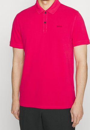 Homme portant un polo à manches courtes rouge vif avec deux boutons noirs et un petit logo noir "BOSS" sur le côté gauche de la poitrine.