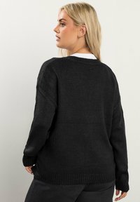 Czarny sweter z dzianiny o luźnym kroju, szerokich rękawach i ściągaczu. Teksturowany materiał z prostym, klasycznym wzorem, idealny do noszenia na warstwy.