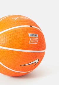 Nike basketball i lys orange med en struktureret overflade, hvide striber og et sort logo. Producentens etiket synlig.