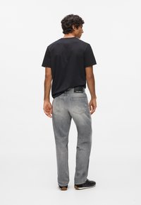 Čierne tričko a svetlo šedé denimové džínsy. Džínsy majú vybledlý vzhľad a zadné vrecká. Čierne topánky s textúrovanou podrážkou.