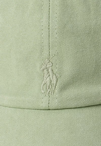 Lys grønn baseballcaps laget av teksturert stoff med et brodert logo av to hester foran.