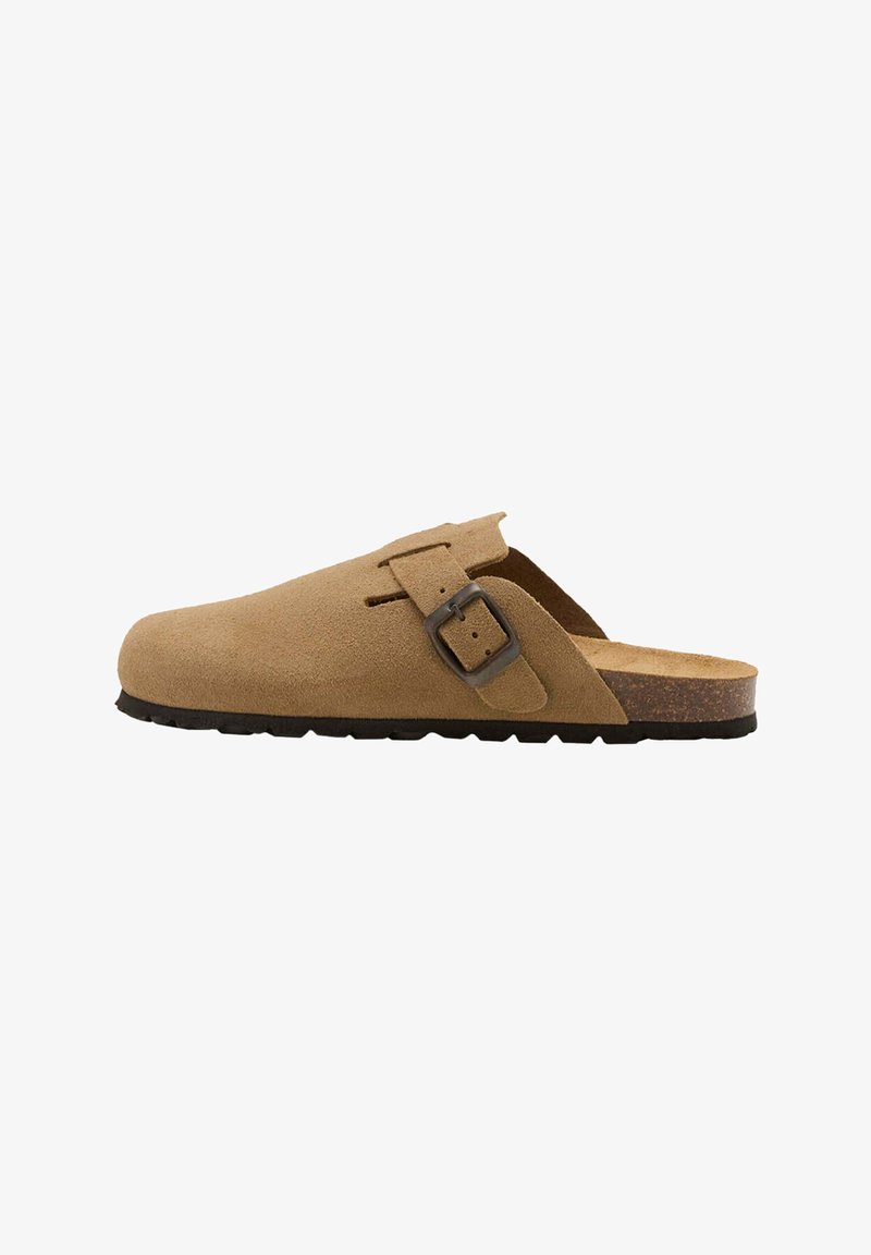 Sabot en daim marron clair à enfiler avec boucle latérale réglable et semelle en caoutchouc noir, montré de profil sur fond blanc.