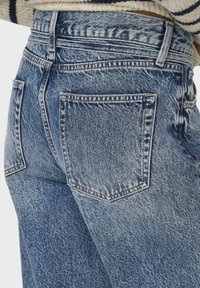 Jeansi din denim de culoare albastră deschisă, cu un finisaj uzat, având două buzunare la spate și talie înaltă. Detaliile de cusătură vizibile îmbunătățesc designul.