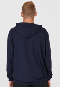Marinblå hoodie med dragsko i huvan, långa ärmar och en avslappnad passform. Slät textur med minimala designelement och inga synliga accenter.