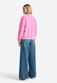 Sweatshirt rose surdimensionné avec un col rond, assorti à un jean en denim bleu à jambes larges avec des poches plaquées et une finition texturée.