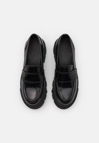 Mocassini neri lucidi con punta arrotondata, suola in gomma e dettaglio in pelle nera sulla tomaia. Texture in pelle liscia con soletta perforata.