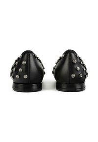 Schwarze flache Schuhe mit runden silbernen Strasssteinen an der Rückseite und an den Seiten, von hinten auf einem weißen Hintergrund gezeigt.