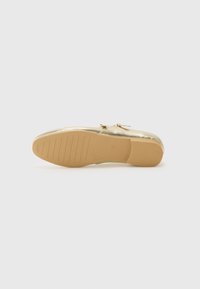 Chaussure style ballerine dorée, avec une surface métallique lisse, un bout arrondi, un matériel minimaliste et une semelle extérieure en caoutchouc texturé.