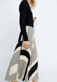 Top nero a maniche lunghe a costine abbinato a una gonna midi plissettata con un design geometrico in bianco e nero.