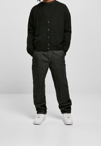 Czarny kardigan z dekoltem w serek i guzikami, zestawiony z luźnymi czarnymi dżinsami z bocznymi kieszeniami. Uzupełnione białymi sneakersami.