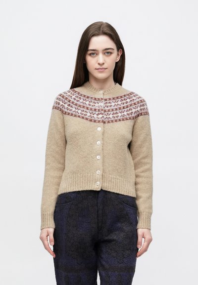 Beige uldcardigan med en cremefarvet og rustfarvet mønstret skulderdel, der har knapper foran og ribkant forneden. Kombineret med mørke mønstrede bukser.