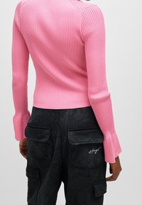 Roze geribd langmouwtop met uitlopende mouwen, gecombineerd met donkere cargobroek met zakken en witte stikdetails.