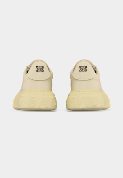 Ζευγάρι μπεζ αθλητικά παπούτσια φαίνονται από πίσω με χοντρές υφασμάτινες σόλες με ανάγλυφο το όνομα της μάρκας και μεταλλικό λογότυπο στην ταμπέλα τη ς φτέρνας.