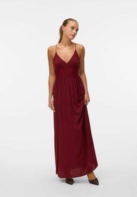 Abito lungo bordeaux con spalline sottili, gonna plissettata e corpetto decorato. Tessuto morbido e fluido che crea un'elegante silhouette.