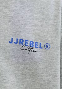 Tissu gris avec le texte « JJREBEL Edition » imprimé, « JJREBEL » en majuscules bleues et « Edition » en cursive noire en dessous.