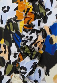 Tissu à motif floral présentant des couleurs vives telles que le bleu, l'orange et le vert, avec une texture froncée d'un côté et une finition lisse.