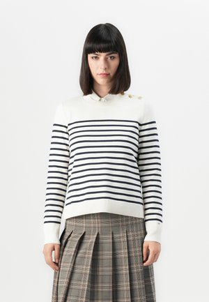 Maglione a righe in crema e blu navy con colletto, dettagli con bottoni sulla spalla e polsini a coste; abbinato a una gonna a quadri.