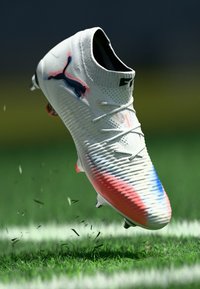 White soccer cleat with a textured mesh upper, featuring a pink and blue gradient at the toe, black logo, and visible laces.