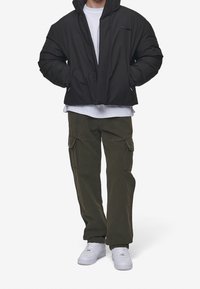 Sort puffjakke med høj krave, parret med olivengrønne cargobukser med sidelommer og hvide sneakers. Minimalistisk design.