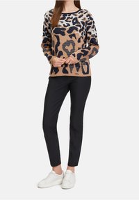 Pull-over imprimé léopard en marron, marine et crème avec une coupe décontractée. Associé à un pantalon noir ajusté et des baskets blanches pour un look casual.