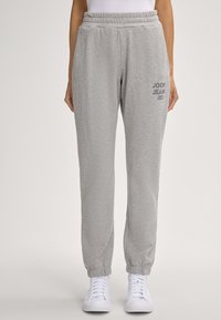Graue Sweatpants aus weichem Baumwollmaterial, mit einem elastischen Bund, Bündchen an den Knöcheln und einem auf der linken Seite gedruckten Logo.
