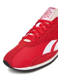 Scarpa da corsa rossa con una combinazione di materiali in camoscio e nylon, con accenti bianchi e suola in gomma testurizzata. Design con allacciatura e marchio.