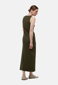 Robe maxi sans manches vert olive avec une silhouette ajustée, texture côtelée et détails de couture, associée à des chaussures plates beige clair.
