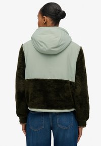 Gewatteerd jack met een lichtgroen bovenstuk en donker groen, pluizig materiaal daaronder. Voorzien van geribbelde manchetten en een losse pasvorm.