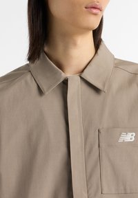 Beige overhemd met knopen en een kraag, zijzak en geborduurd wit logo. Gladde stof met minimale naden en een gestructureerd ontwerp.