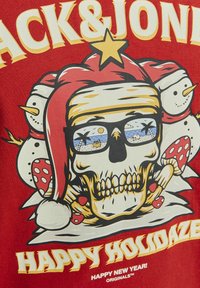 Camiseta roja con un diseño gráfico de un cráneo con un gorro de Santa, rodeado de muñecos de nieve y setas, con el texto "HAPPY HOLIDAZE".