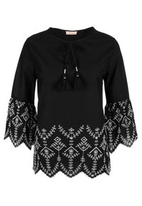 Blouse noire avec manches évasées ornées d'une broderie blanche délicate le long de l'ourlet. Fermeture à nouer avec pompons au niveau du col. Tissu doux et texturé.