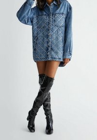 Denim oversized shirt jacket featuring diamond-patterned embellishments, contrasting black glossy thigh-high boots with a pointed toe.