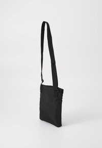 Borsa a tracolla nera realizzata in tessuto liscio, con una tracolla regolabile e una forma semplice e rettangolare senza hardware visibile.