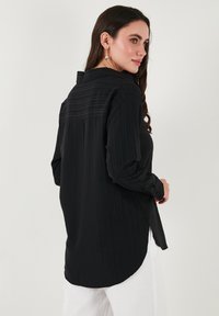Black long-sleeve shirt with textured stripes, a collared neckline, and button cuffs. Rounded hem and loose fit for comfort.