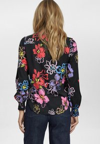 Blusa nera a fiori con maniche lunghe, caratterizzata da vivaci fiori rossi, rosa, blu e viola. Polsini elasticizzati e vestibilità rilassata.