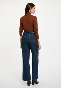 Pantalon en denim bleu foncé taille haute avec une jambe large, doté de poches arrière et d'une texture lisse, associé à un haut marron ajusté.