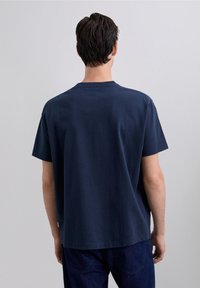 Donkerblauw katoenen T-shirt met korte mouwen, een ronde hals en een losse pasvorm, gezien vanaf de achterkant. Heeft een klein label vlakbij de taille.