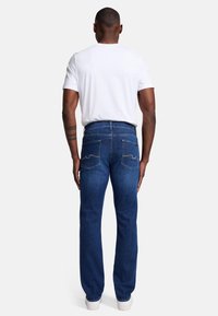 Niebieskie dżinsy z prostymi nogawkami, tylne kieszenie z haftowanym wzorem, noszone z klasyczną białą koszulką i białymi trampkami.