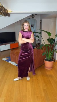 Velvet, dark purple maxi dress with a high slit and cap sleeves. Model poses with arms crossed, paired with white slip-on shoes.