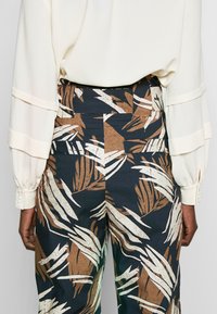 Blommönstrade byxor i nyanser av brunt, kräm och marinblå; hög midja med en slät textur och bakfickor.